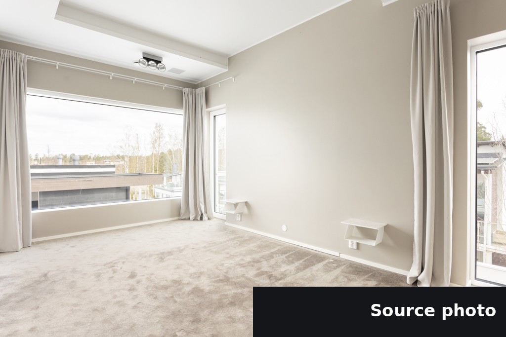 An empty carpeted room with large windows and curtains, the original listing photo.